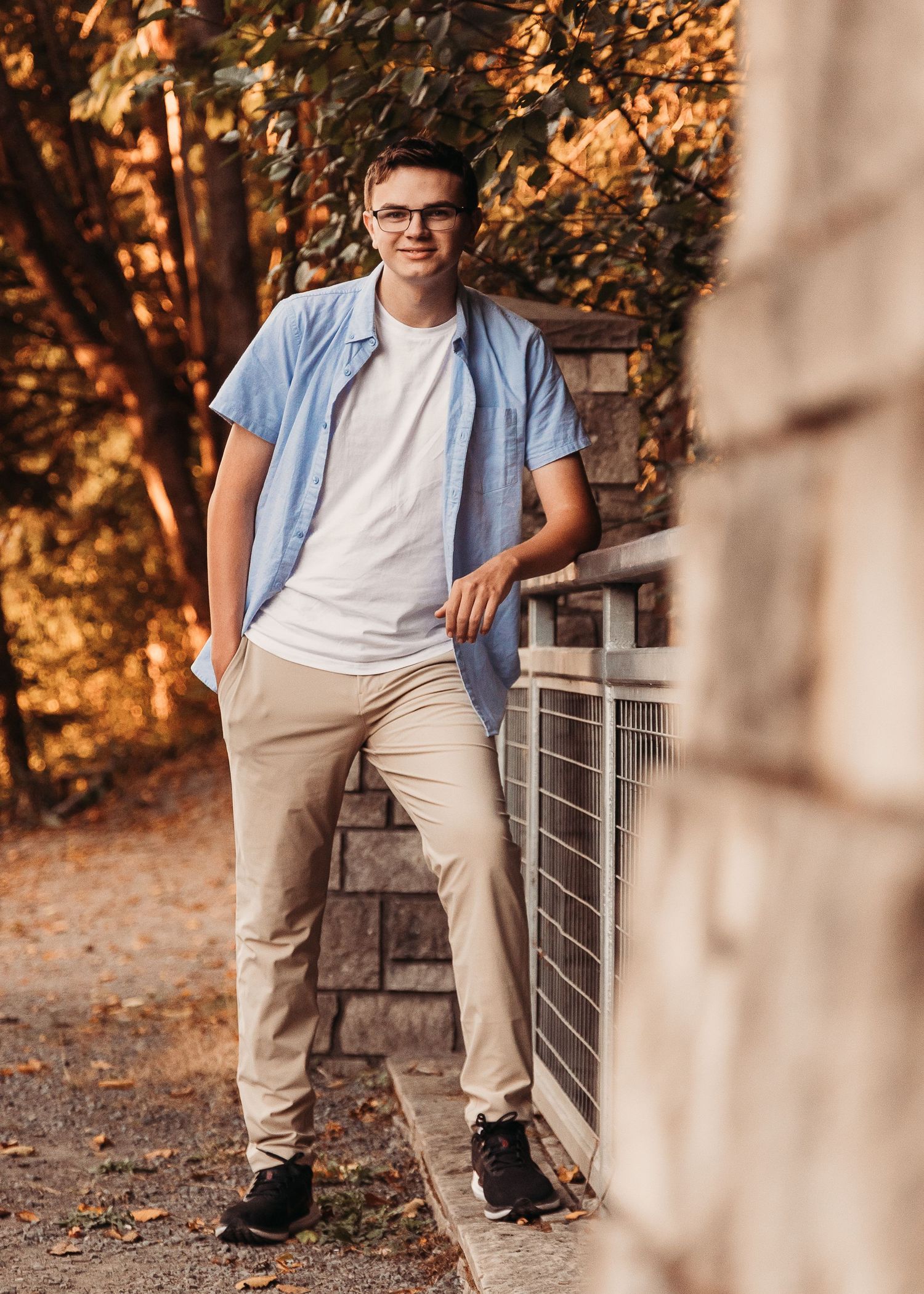 Casual outdoor portrait with light blue shirt, white t-shirt and khaki pants against autumn foliage in warm sunlight.