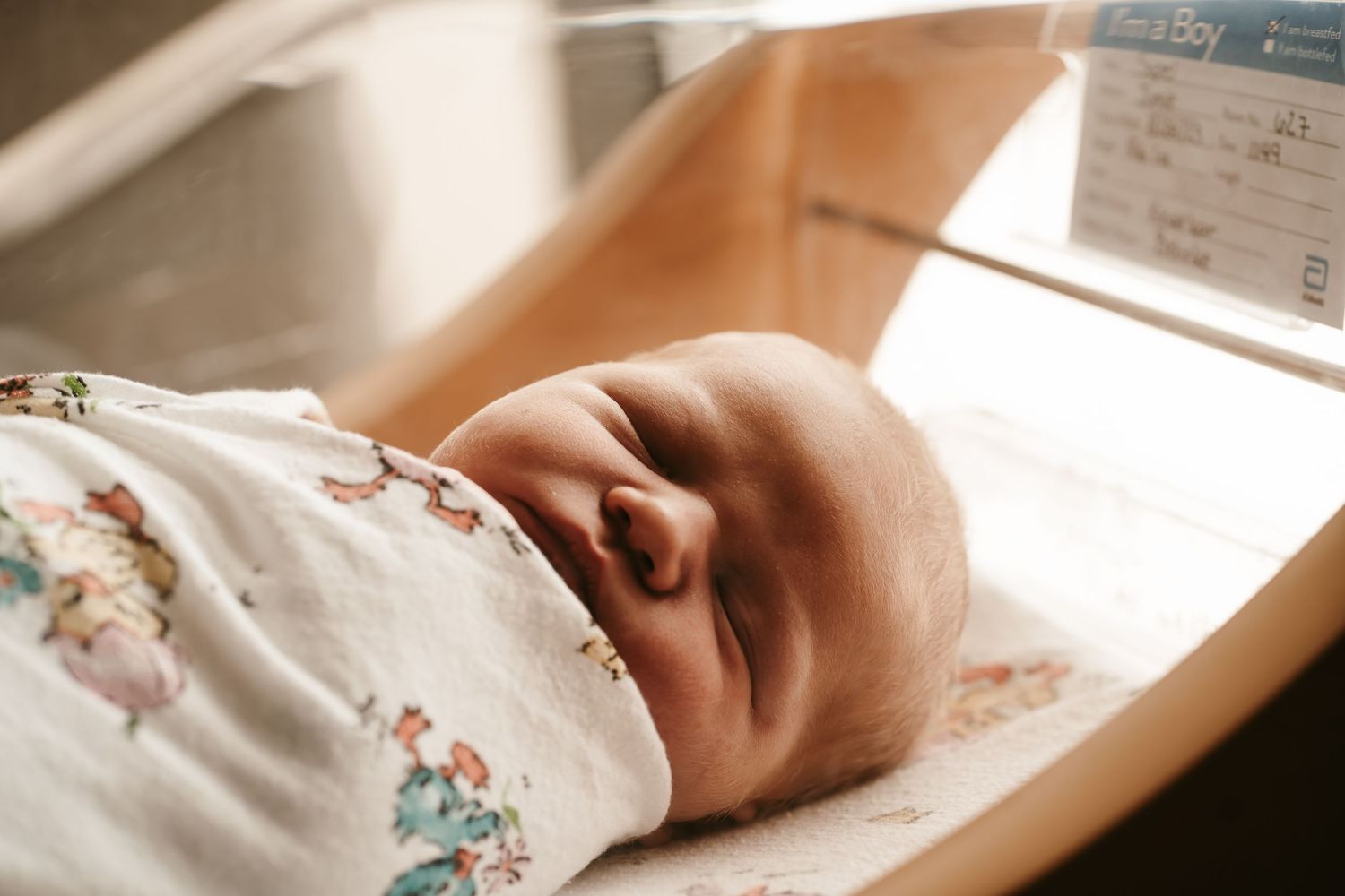 Sleeping newborn in floral print outfit resting in warm natural light.
