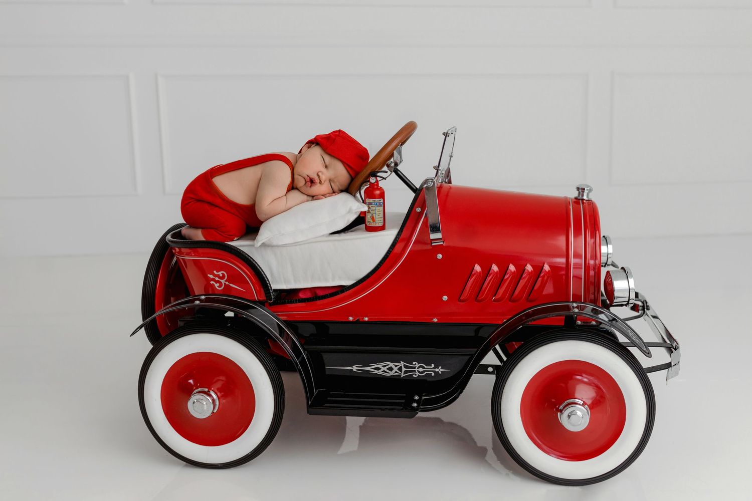 Vintage red pedal car with white trim and red wheels against a white background. NEWBORN PHOTOGRAPHY, FIREMAN THEMED NEWBORN SESSION, NEWBOR