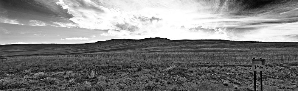 Black and white panoramic landscape of rolling prairie hills under dramatic cloudy sky in rural grasslands.