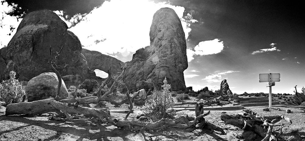 A dramatic black and white landscape of Arches National Park with towering rock formations against a cloudy sky.