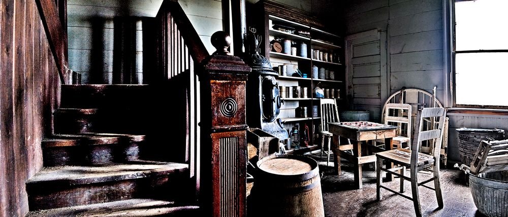 Vintage wooden staircase and rocking chair in an old farmhouse interior with rustic bookshelves and wooden furnishings.