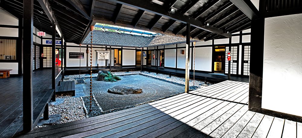 Traditional Japanese zen garden with raked gravel patterns and wooden deck walkway inside a minimalist temple courtyard.