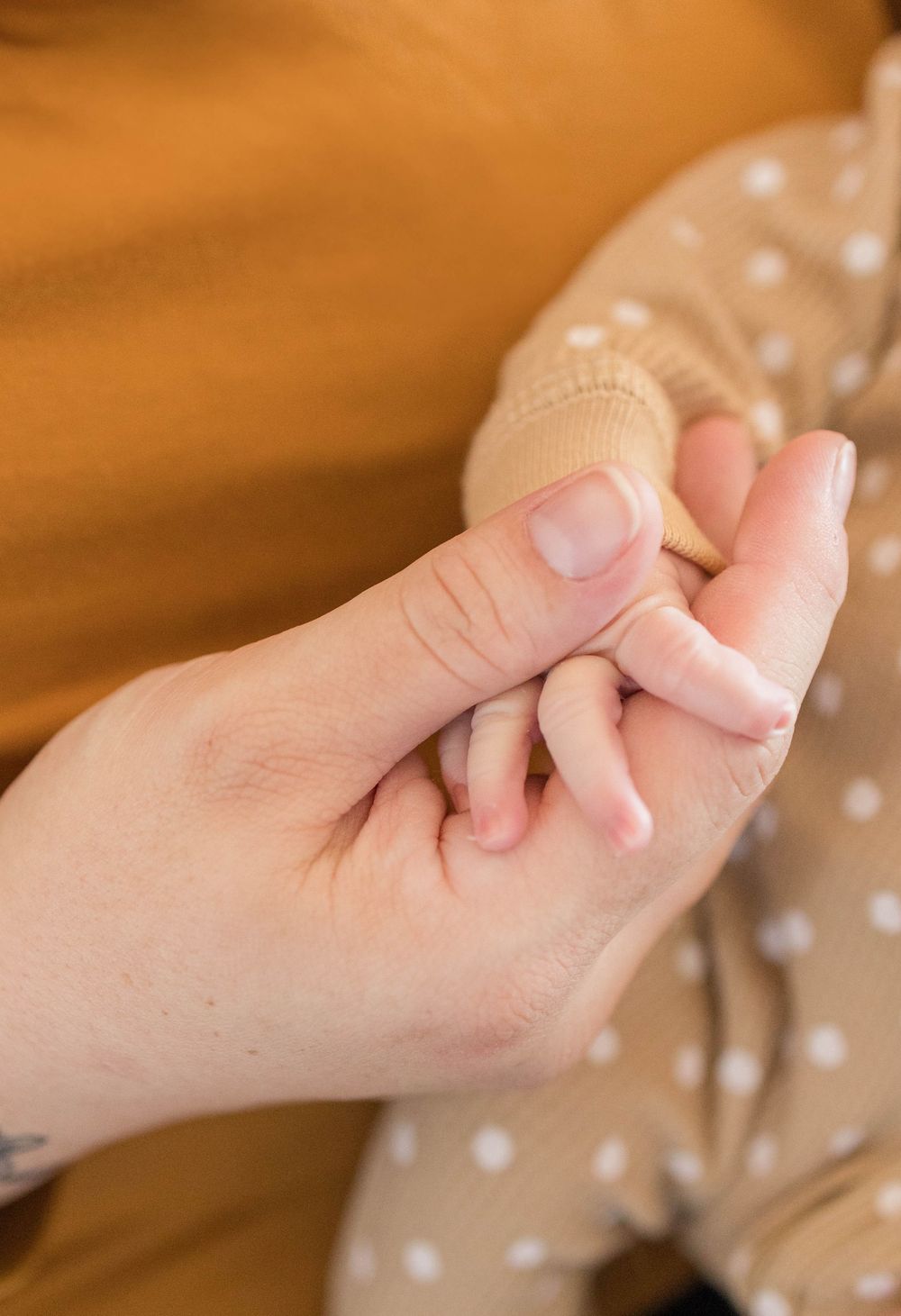 A close-up view of a tiny baby's hand being gently held by an adult finger against a soft brown background.