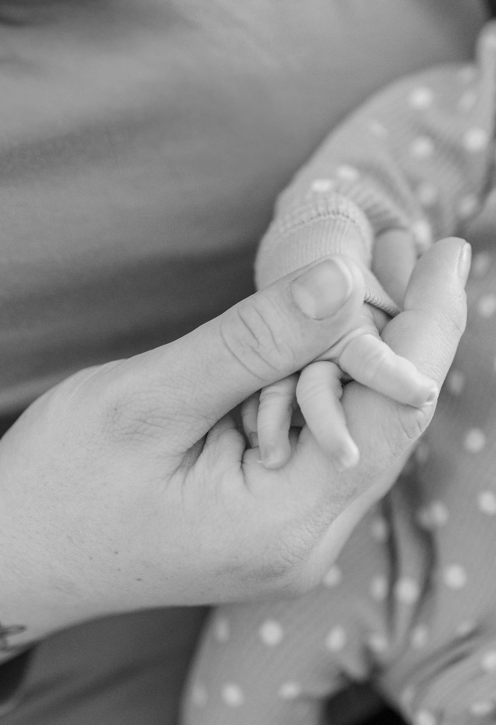 Close-up black and white shot of an adult hand tenderly holding a baby's tiny hand.