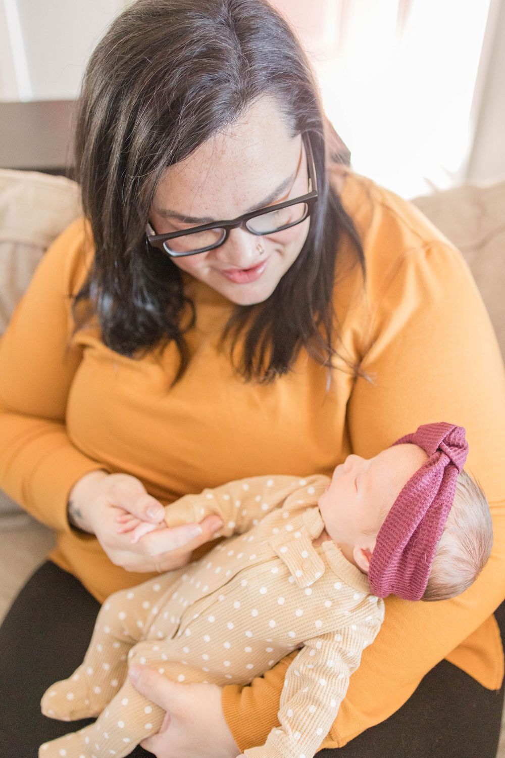 Caregiver in yellow sweater holding and lovingly interacting with a baby wearing polka dot onesie.