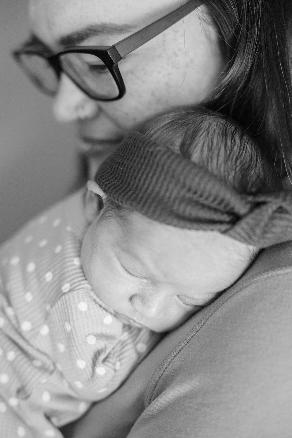A tender black and white photo of wearing glasses and holding a sleeping baby in polka dot clothing.