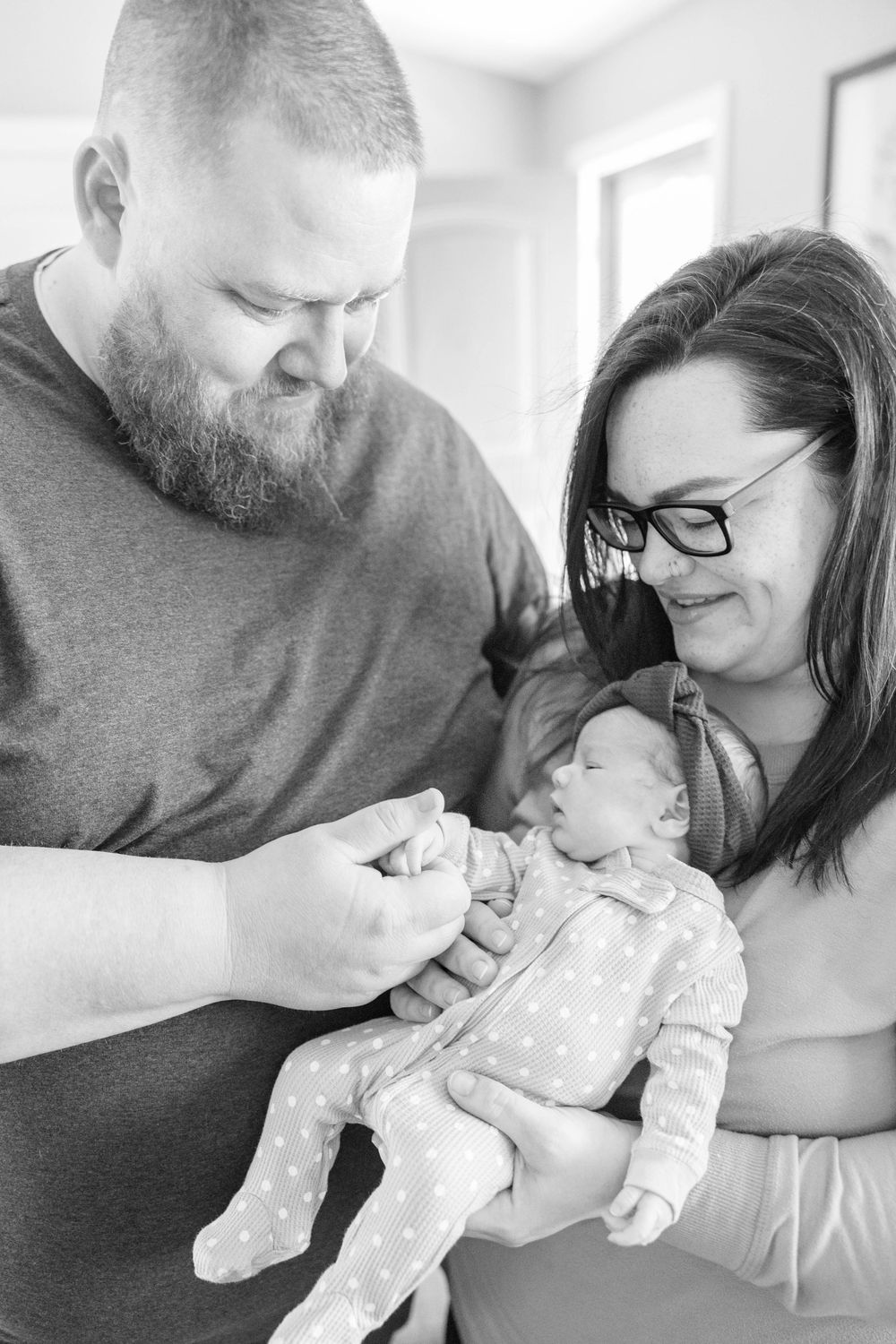 Couple gazes lovingly at their baby wearing polka dot pajamas during an intimate indoor photo session.