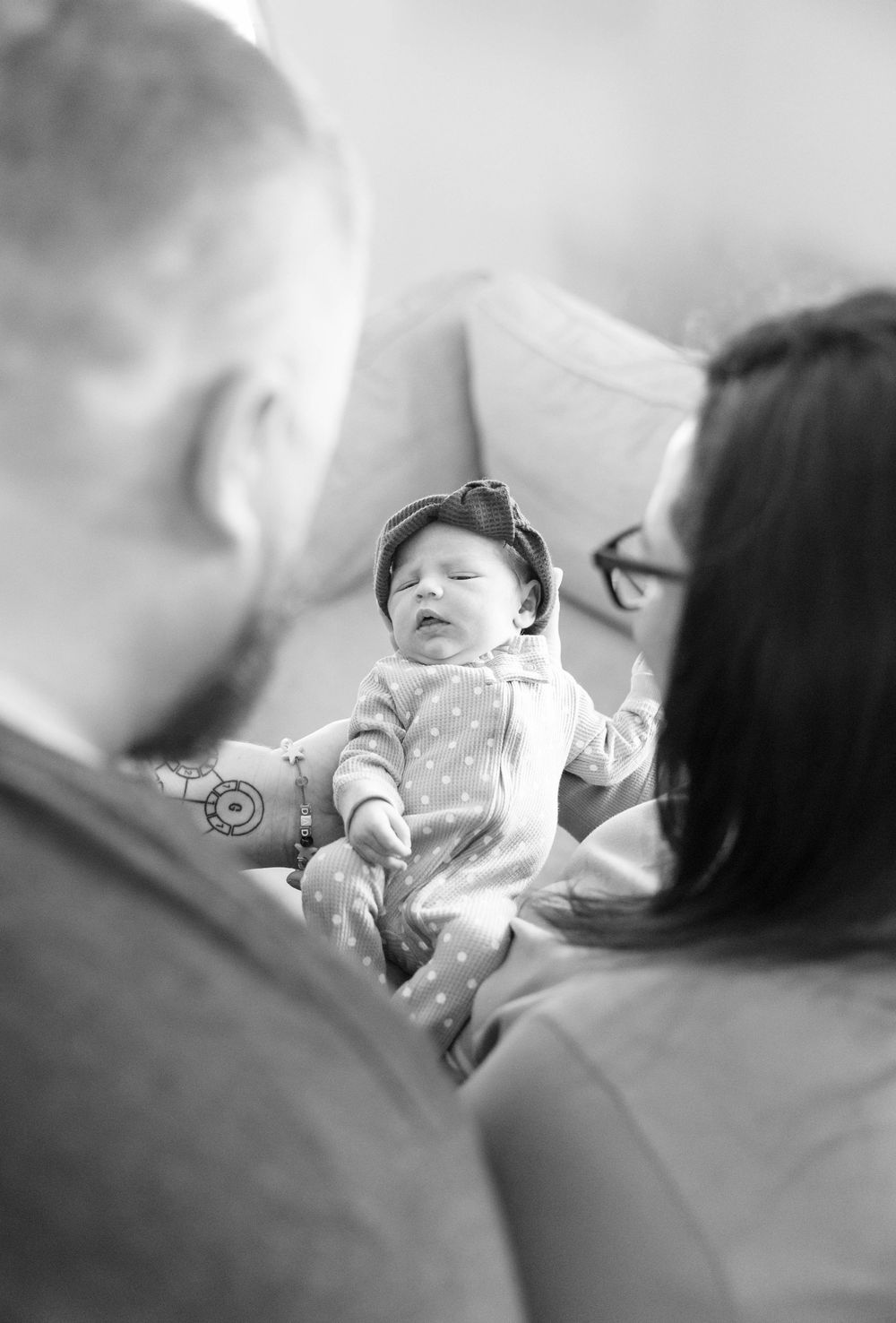 A black and white photograph of parents admiring their infant dressed in polka dot clothing.
