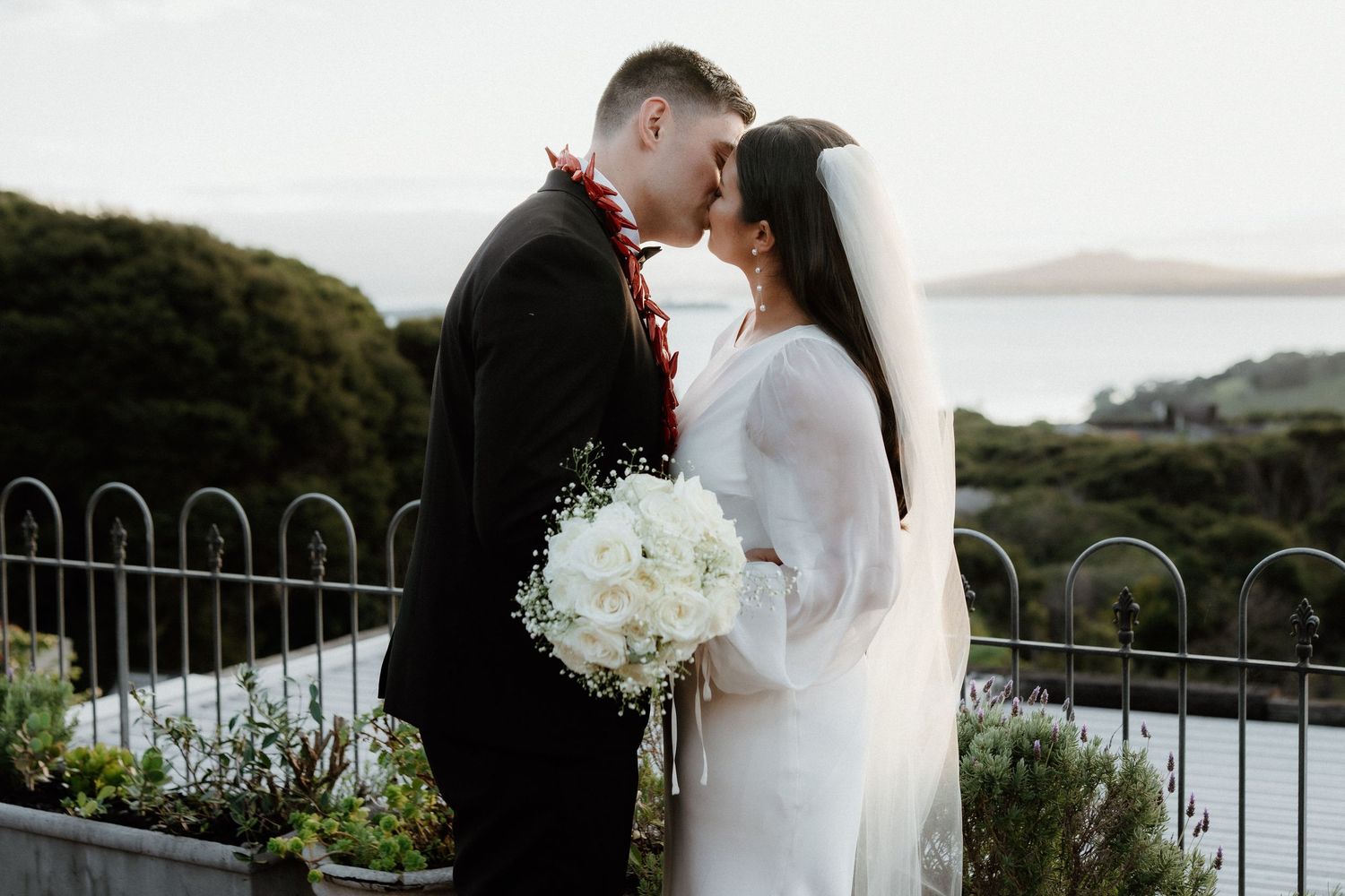 A romantic wedding couple shares a tender moment on a scenic overlook with rolling hills and a white bouquet.