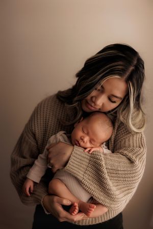 A parent in a cozy beige sweater cradles and gazes lovingly at their sleeping newborn baby.