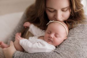 Sleeping newborn in white onesie rests peacefully on soft gray sweater during intimate bonding moment.