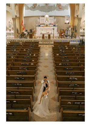 Wedding photographer captures bride in white gown walking down church aisle between wooden pews.