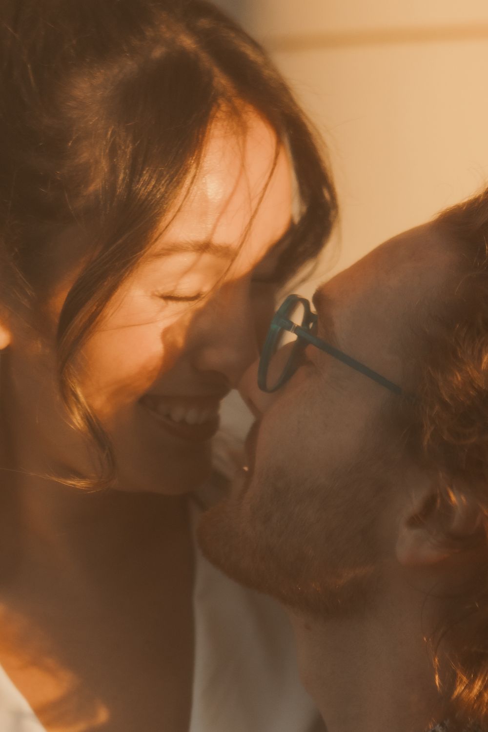 Intimate close-up photo of couple about to kiss in warm glowing sunlight through window.