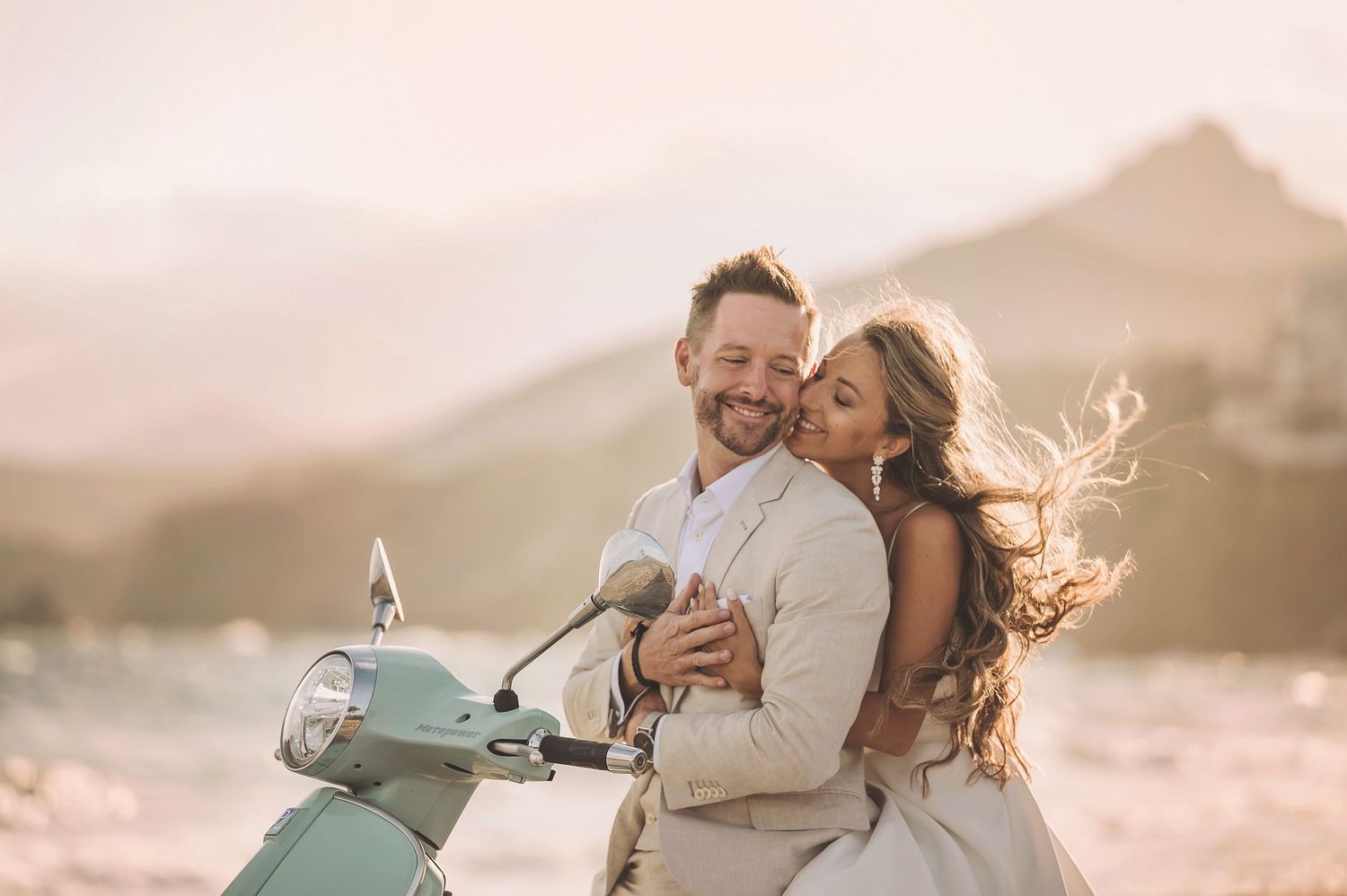 Romantic couple sharing a joyful moment on a vintage scooter against a mountainous sunset backdrop.