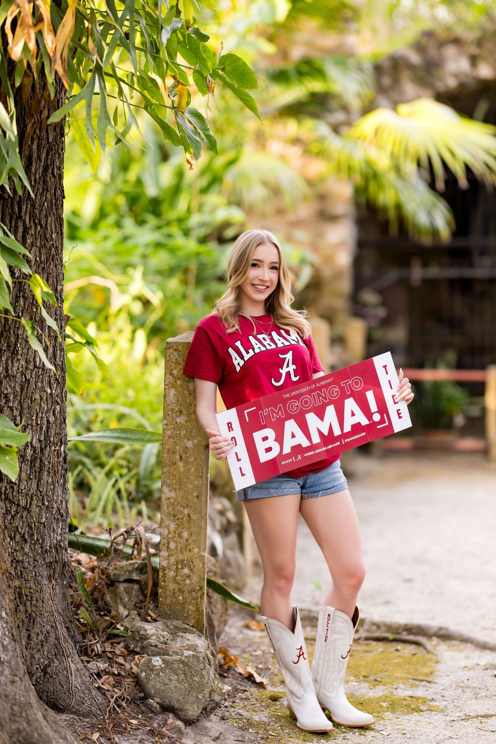 Person in Alabama team gear and white boots poses with Bama spirit signs on a stone pathway.