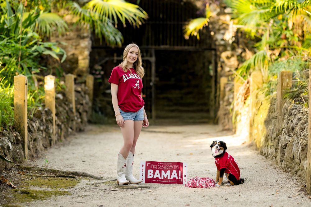 Alabama fan with a small black and white dog and Bama signs on a garden path.