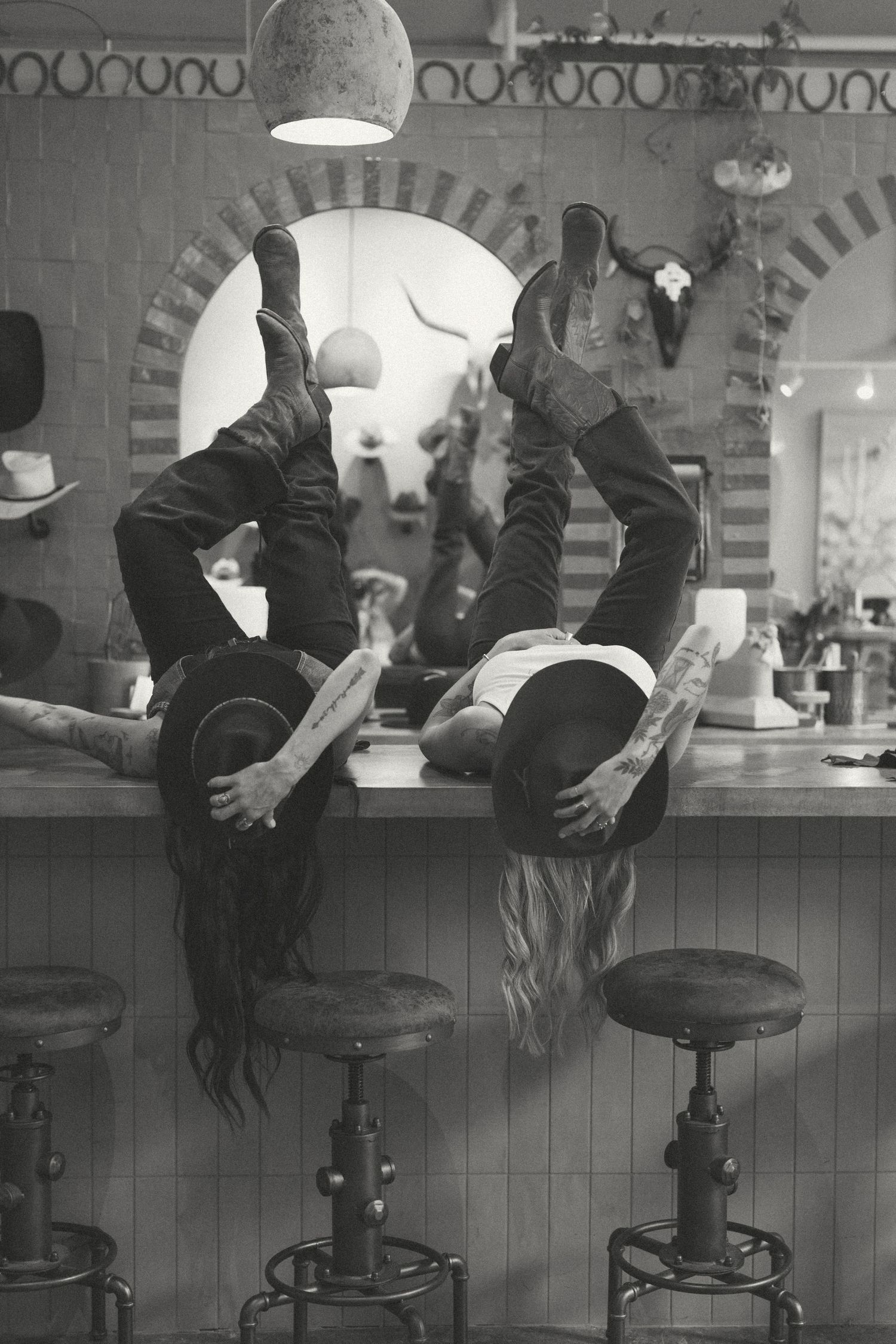 Two people perform acrobatic handstands on bar stools at a retro-style diner counter in black and white photography.