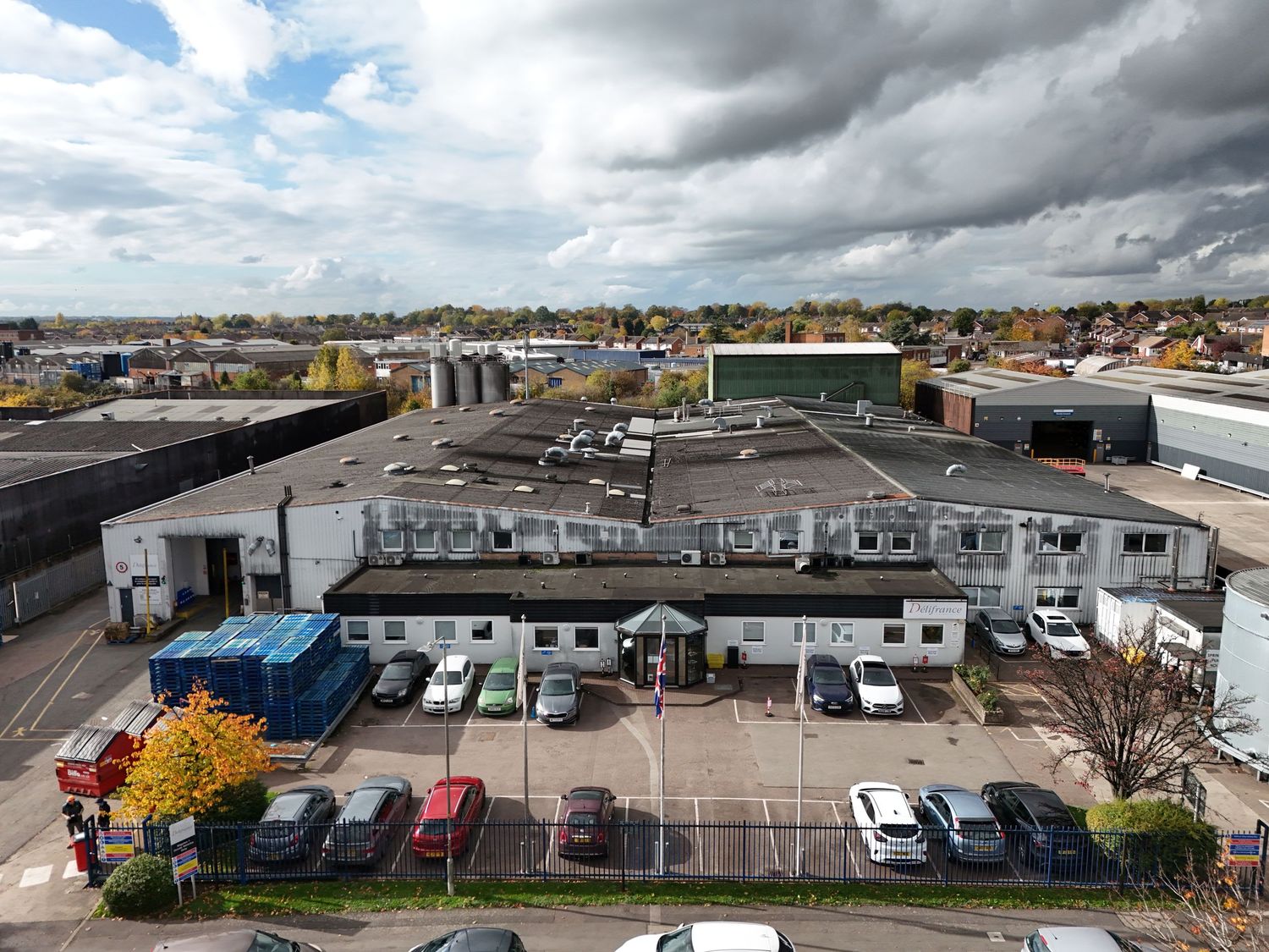 Aerial view of commercial buildings and parking lot with cars under dramatic cloudy sky in urban setting.