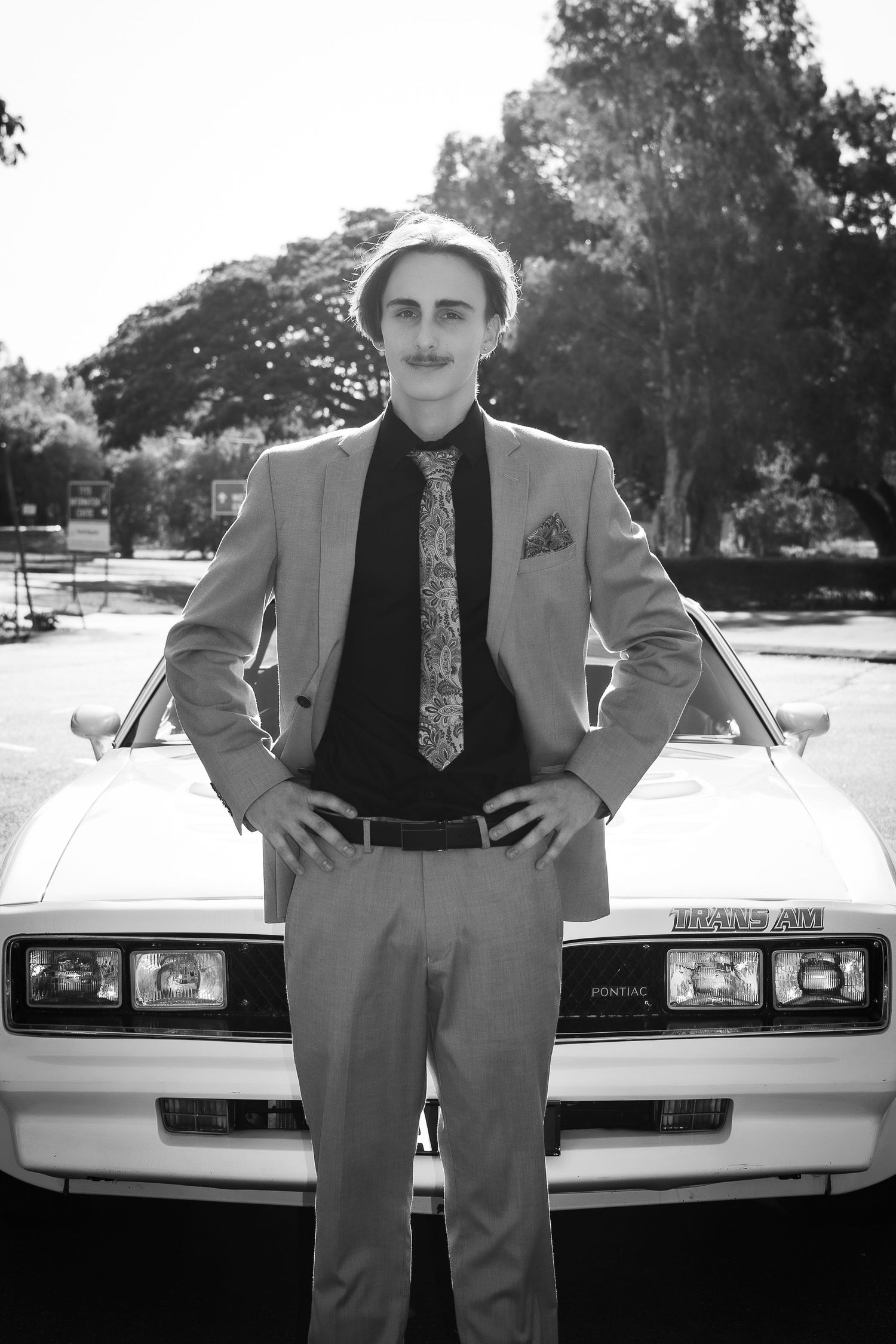 Black and white photo series of a person posing in a suit and tie next to a white classic car.