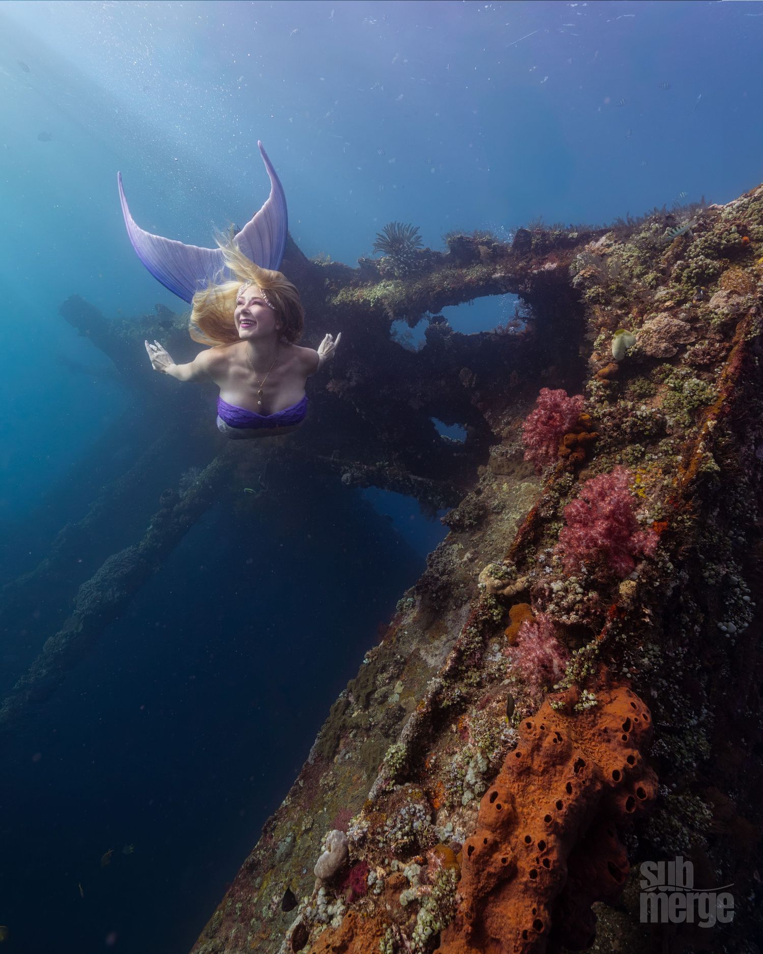 Underwater sequence of a diver in white floating gracefully near a rocky reef wall in deep blue ocean waters.
