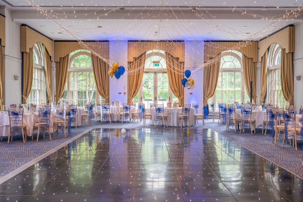 Large banquet hall with blue accent lighting and rows of formal dining tables.