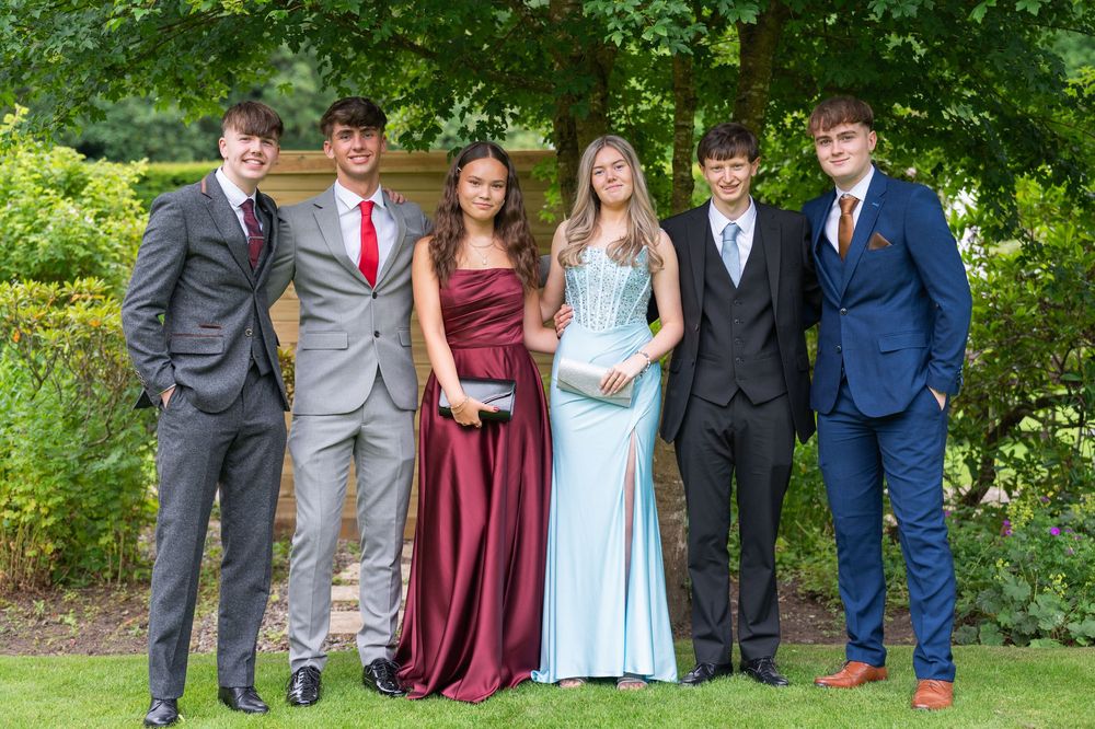 Formal group photo of people in suits and dresses posed together outdoors.