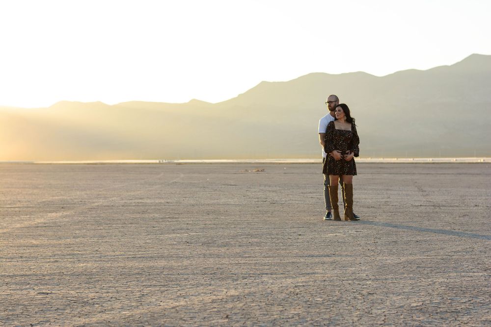 A couple stands together on the vast white salt flats of Bonneville during sunset with mountains in the distance.