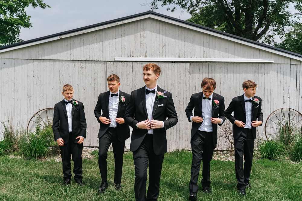 A sequence of six photos showing groomsmen in black tuxedos posing playfully against a white barn wall.