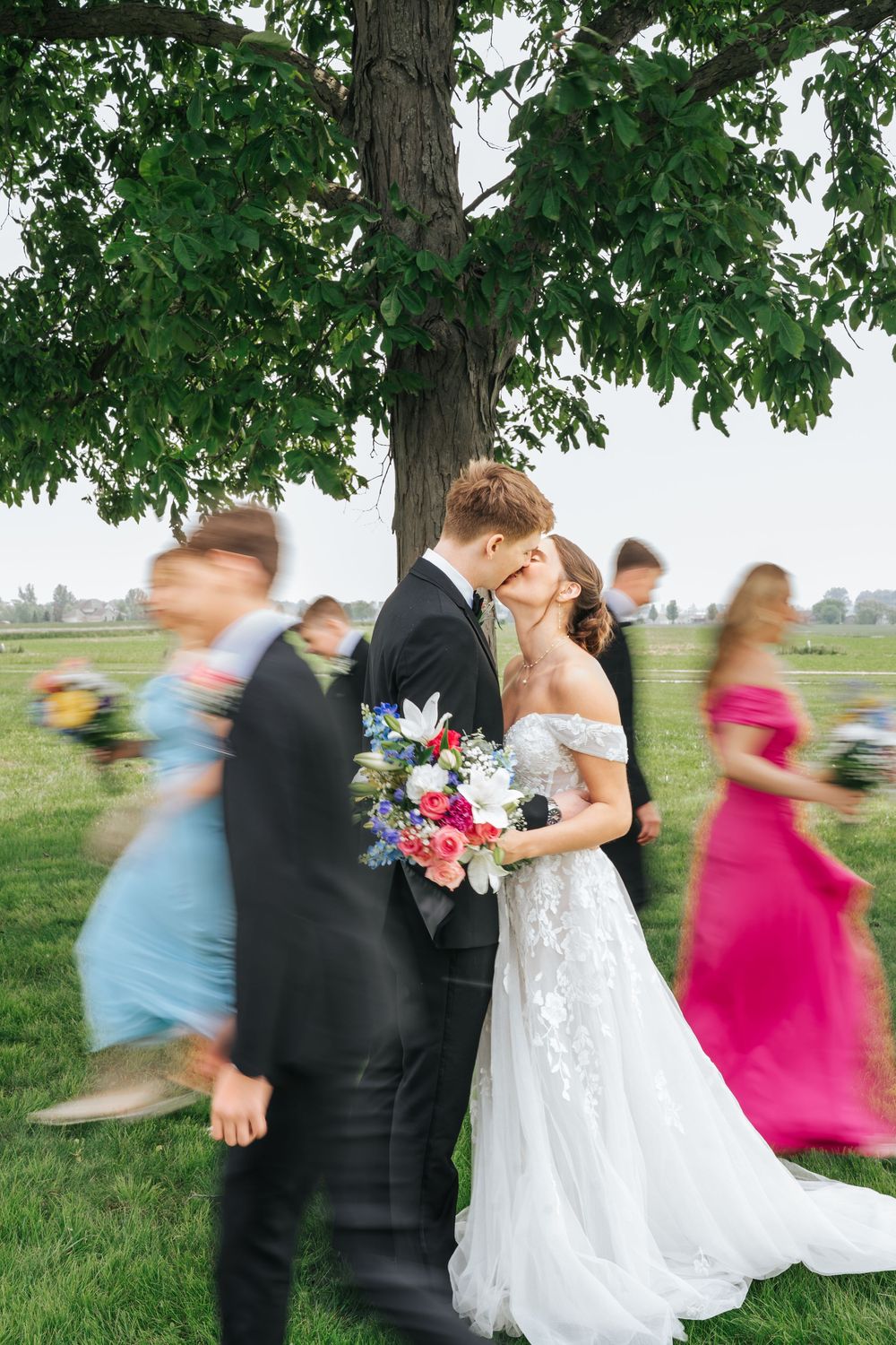 Motion-blurred wedding party spins and dances outdoors under a tree in a playful photo sequence.