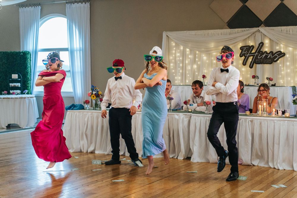 Wedding party members wearing blindfolds dance together at a reception with twinkle lights in the background.