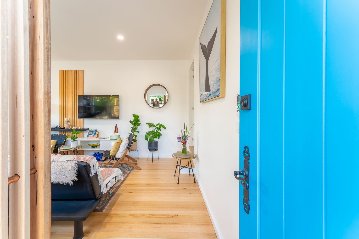Bright modern interior hallway with striking blue front door opening to spacious light-filled living room.