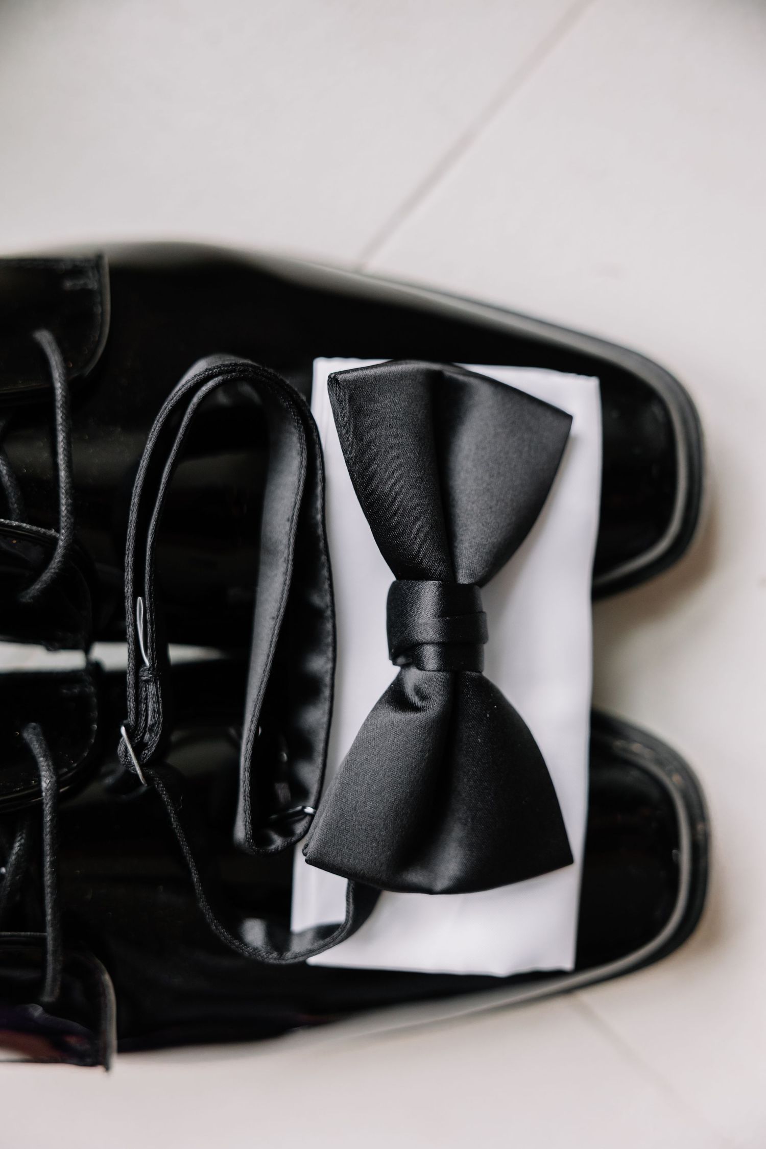 Black formal dress shoes with matching bow tie on white surface.