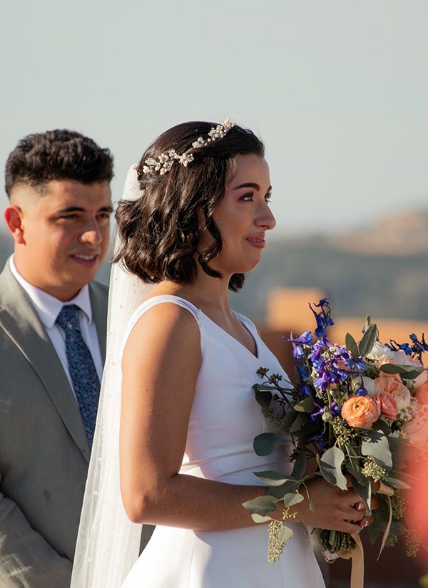 Bride and brother standing side by side with bouquet during sunny outdoor wedding ceremony