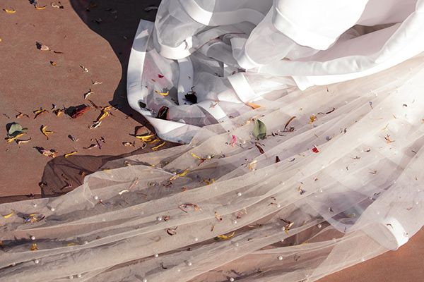 Detail shot of bride’s veil and dress train scattered with petals after wedding ceremony