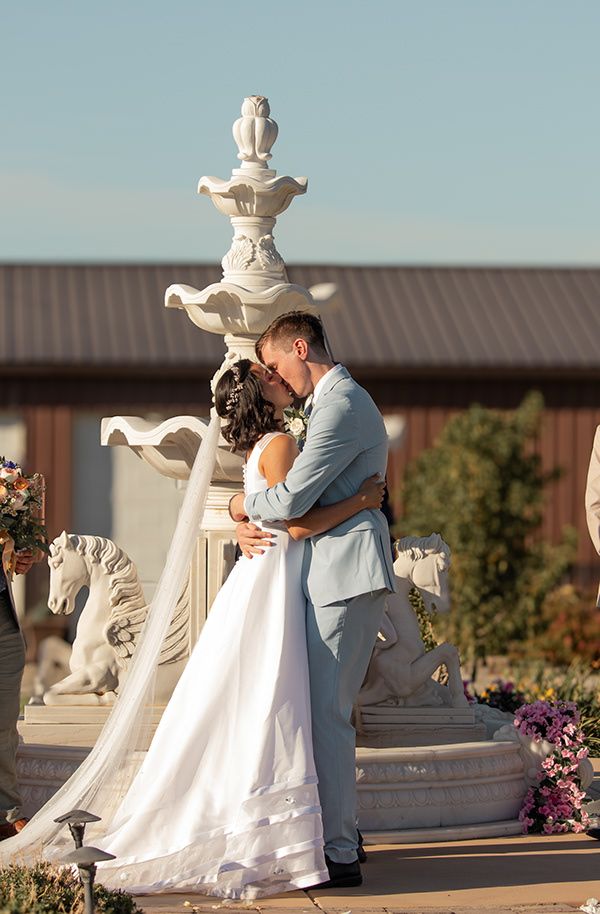 Bride and groom share their first kiss in front of a fountain during outdoor wedding ceremony in Tri-Cities WA