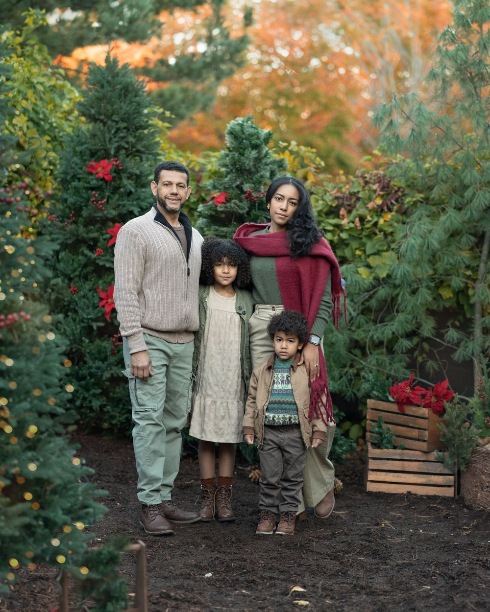 Family enjoying a fall day together in a garden with red roses and autumn foliage in the background.