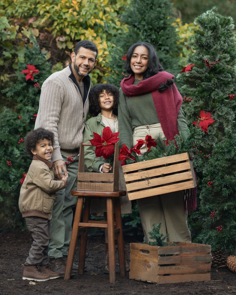 A family shares a joyful moment together in a garden with blooming red roses and wooden crates.