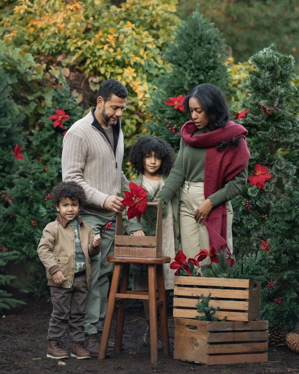 A family decorates wooden crates with red poinsettia flowers in a garden during the holiday season.