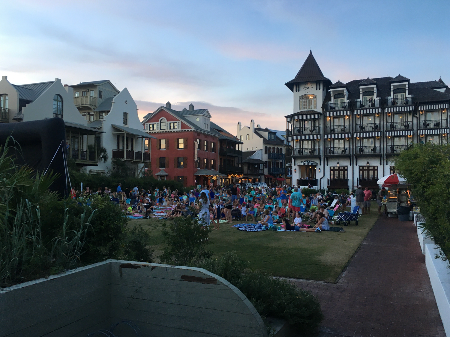 A panoramic view of beachfront houses and crowds gathered on the shore at dusk.