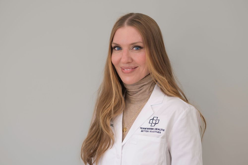 Healthcare provider in white lab coat with long hair against neutral background.