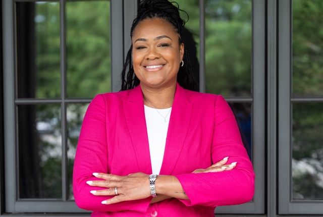 Professional branding portrait of a smiling businesswoman wearing a bright pink blazer with her arms crossed in front of glass doors.