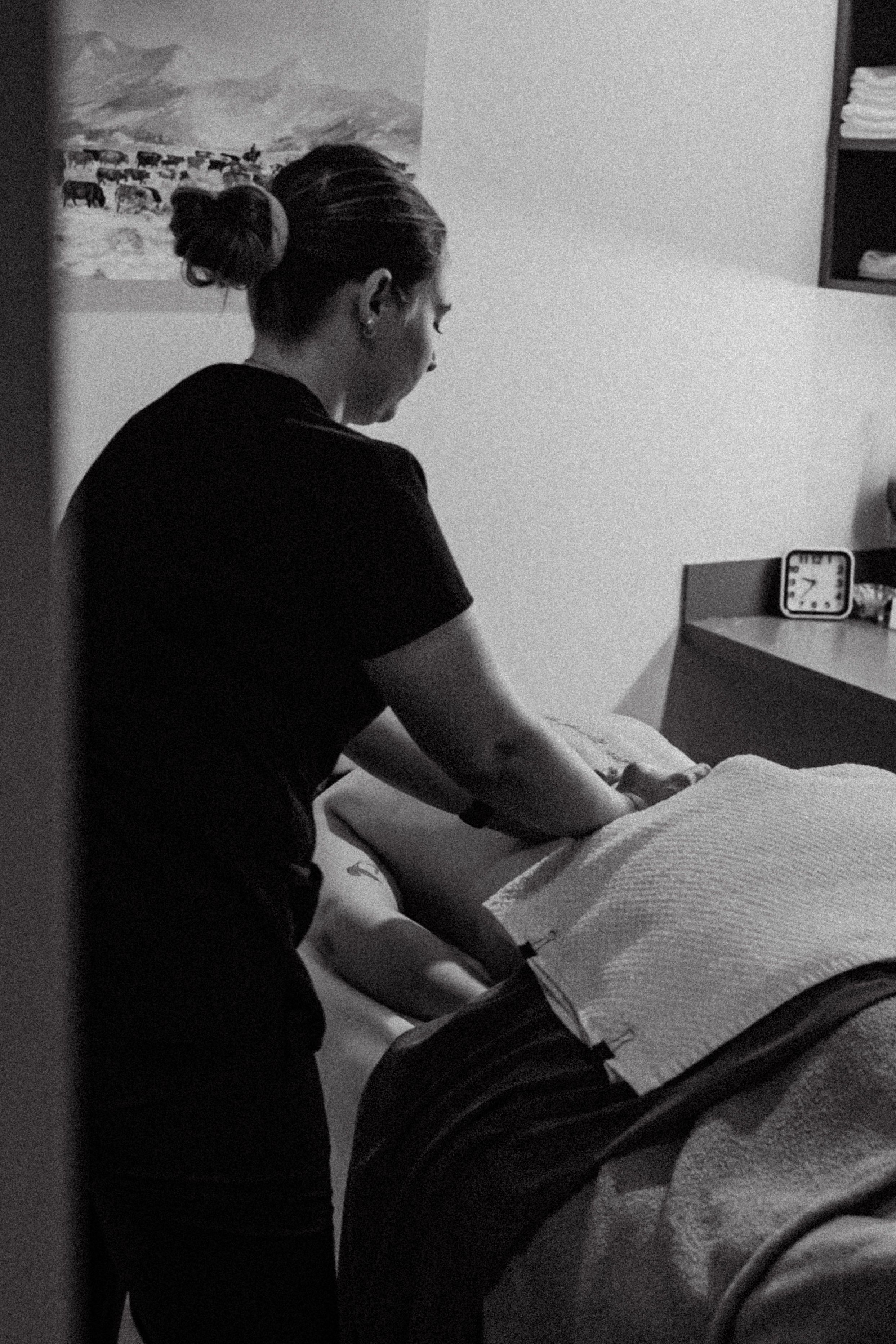 A massage therapist in black attire performs a therapeutic treatment on a client lying on a massage table.