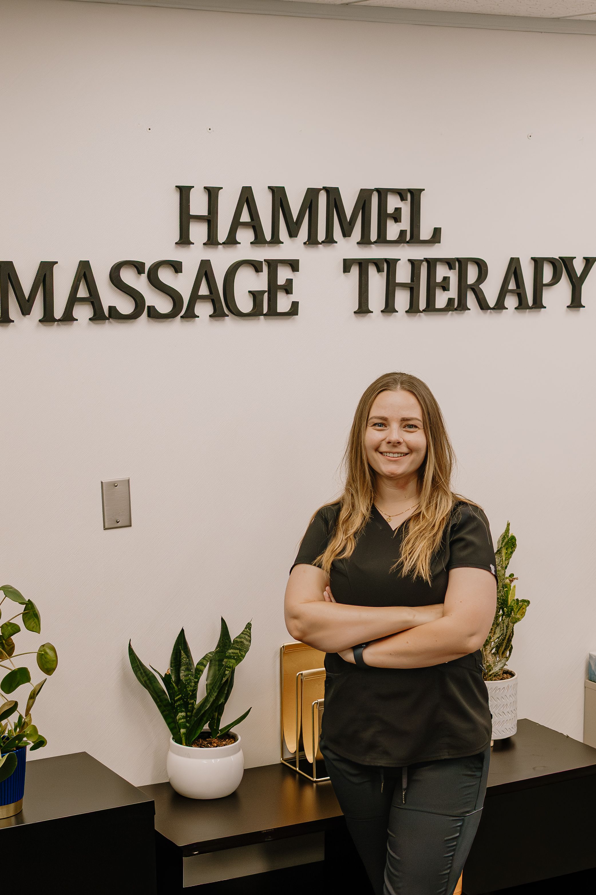 Massage therapy office interior with white walls, black trim, and decorative potted plants on a ledge.