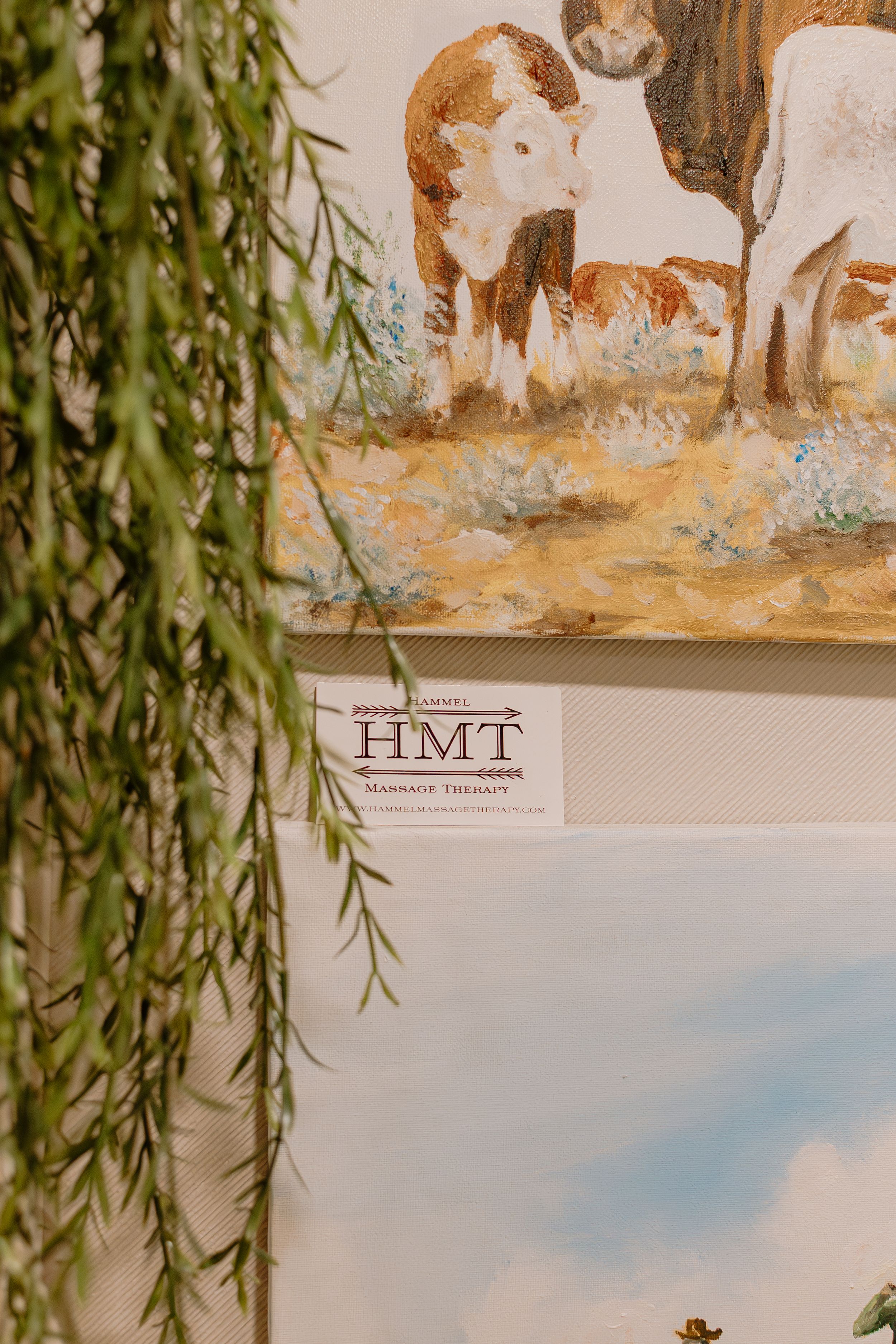 Artwork display on a wall with willow branches hanging down in the foreground.