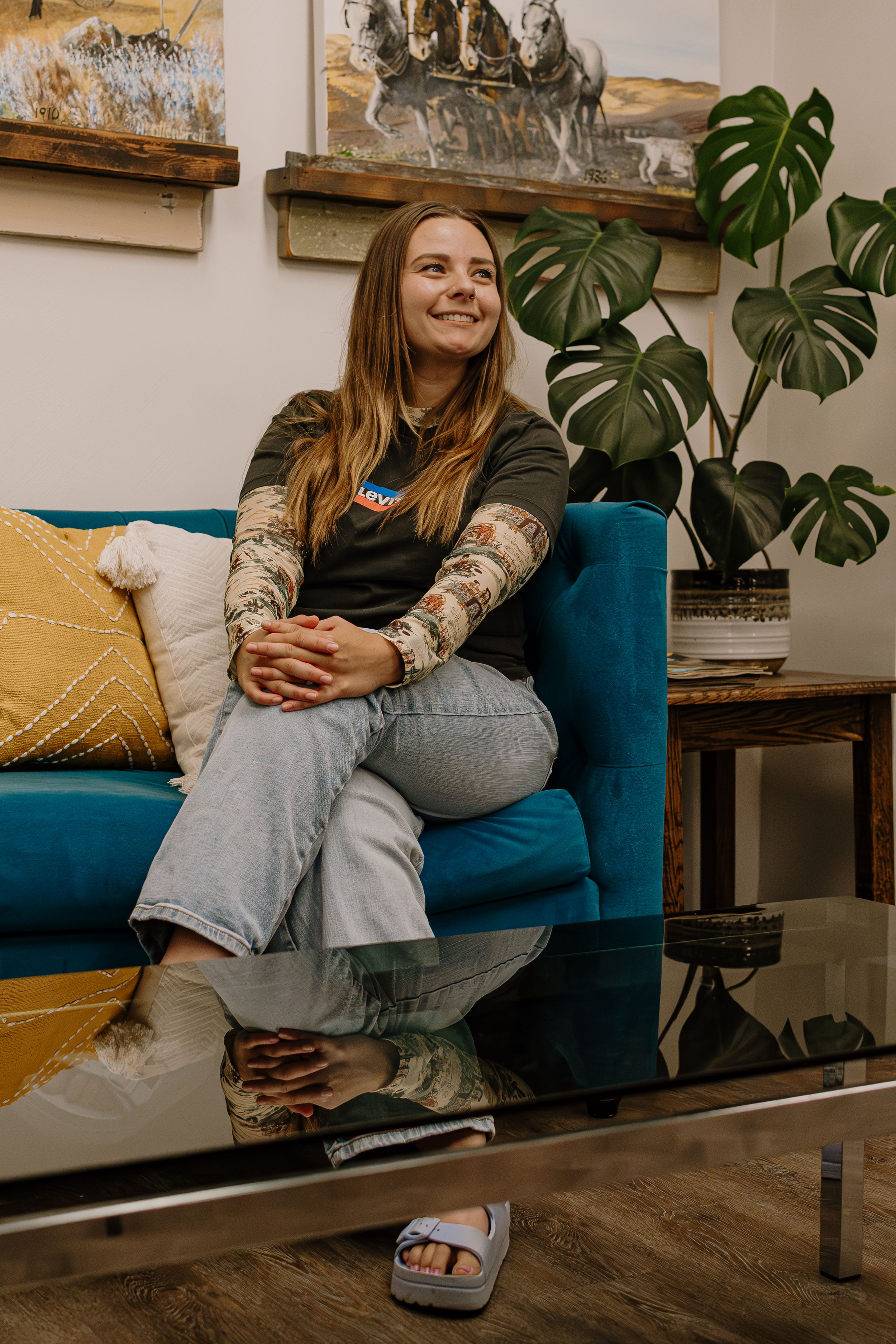 A person relaxes on a blue couch with monstera plants and artwork in a cozy living room setting.