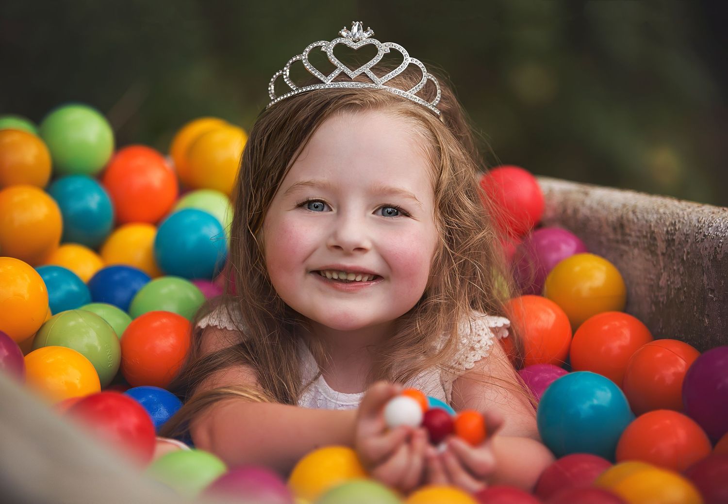 Child plays in colorful ball pit with bright plastic spheres in red, yellow, blue and orange.