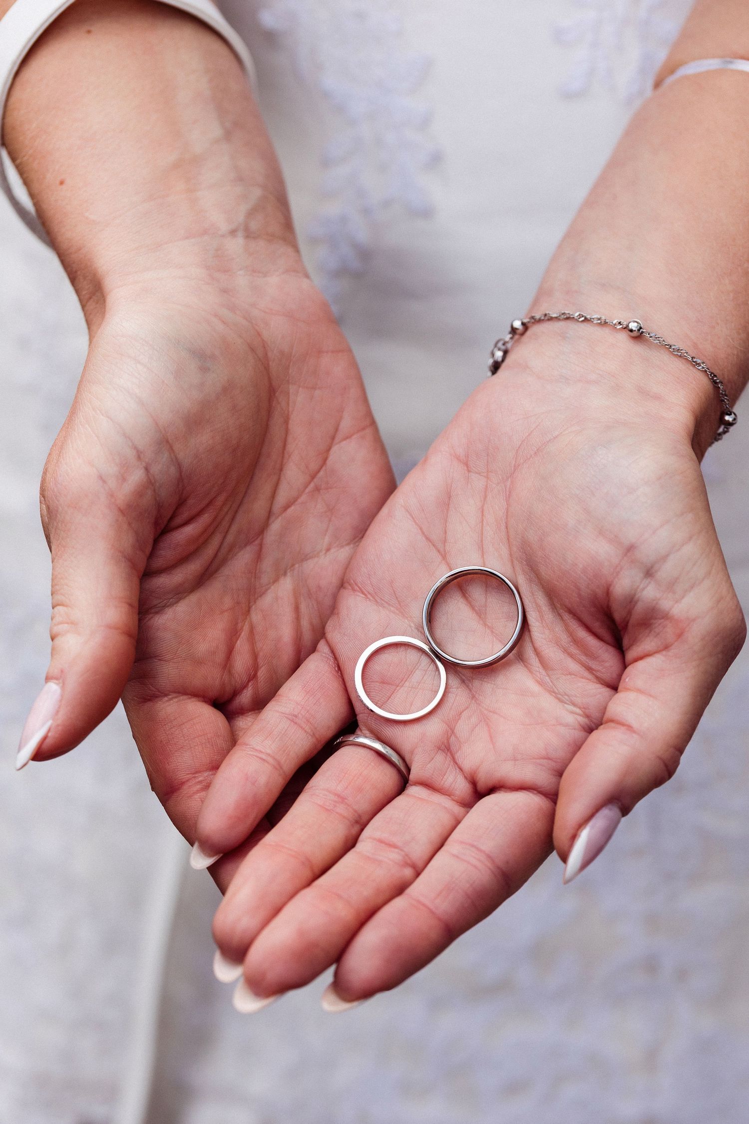 A sequence of hands holding a silver ring against a white marble background shows different angles of the jewelry piece.