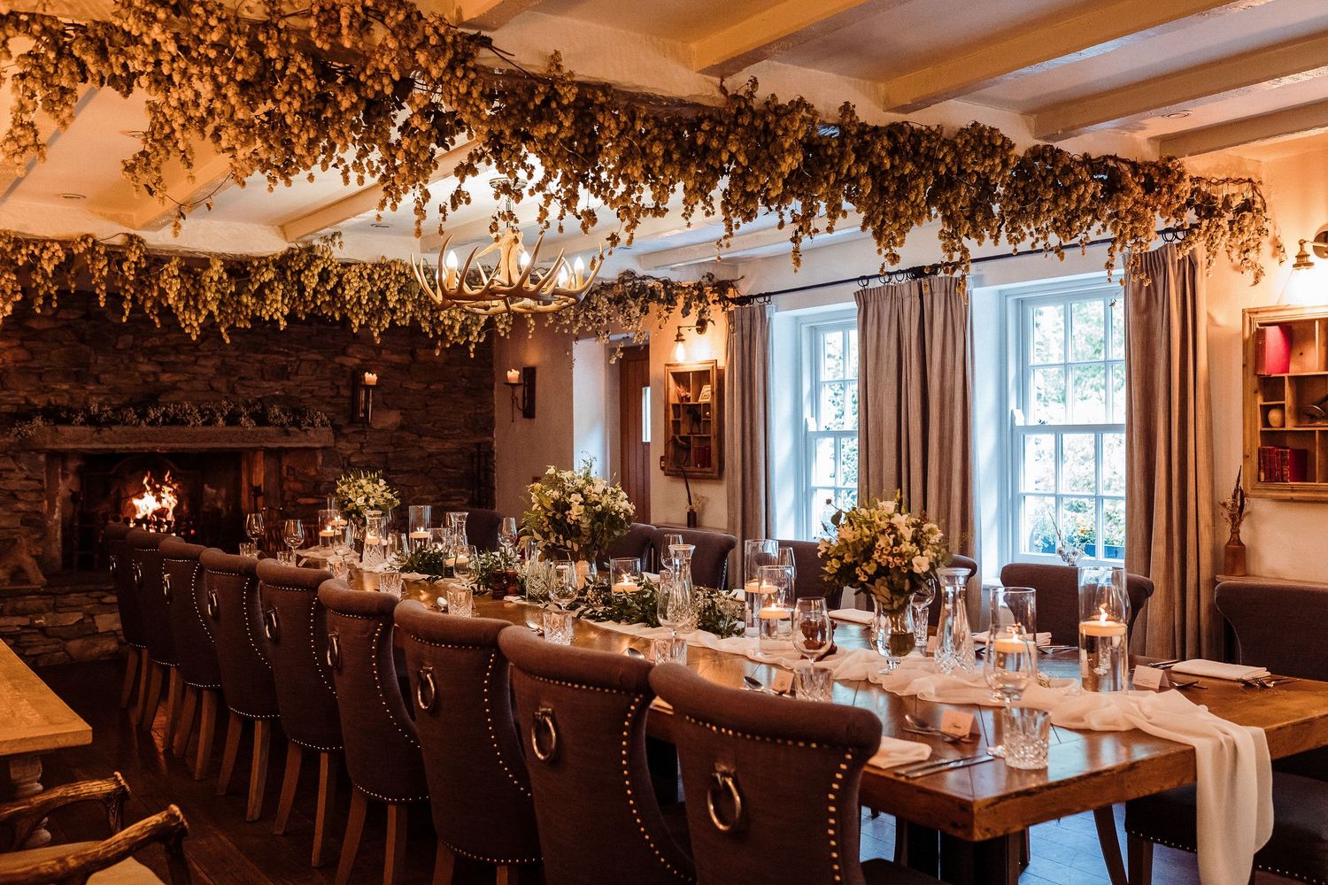Elegant dining room with long wooden table, crystal chandelier and rustic dried floral arrangements hanging from ceiling.