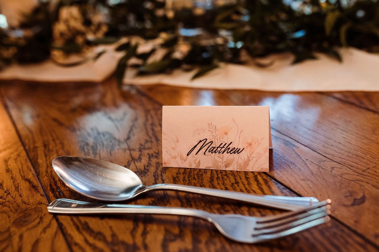Place setting with silver cutlery and handwritten name card on wooden table.